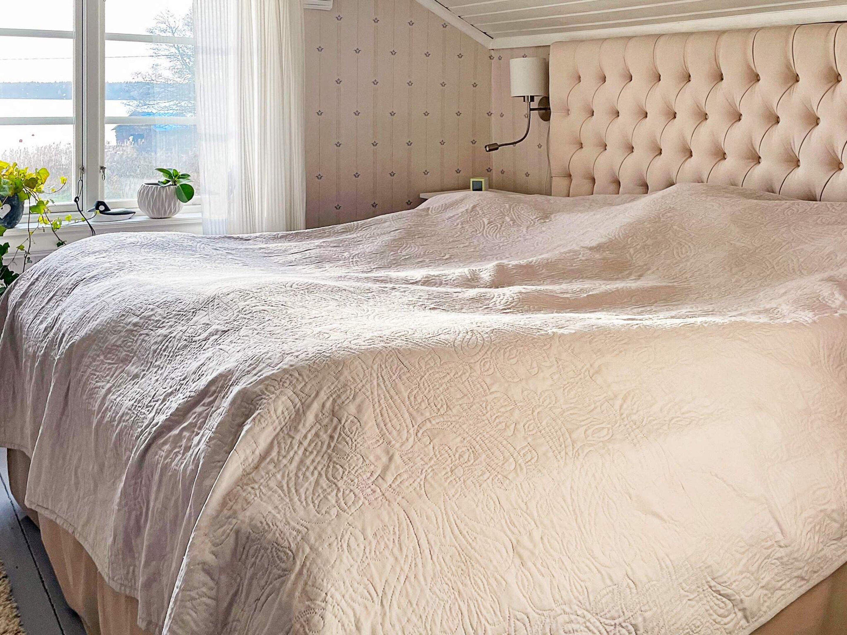 Un dormitorio con una cama grande, una ventana con cortinas y una lámpara fijada a la pared.