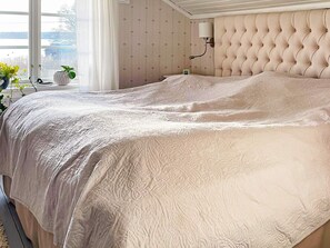 A bedroom with a large bed, a window with curtains, and a wall-mounted lamp. - 5 Star Holiday Home in Bjorko (Björkö)