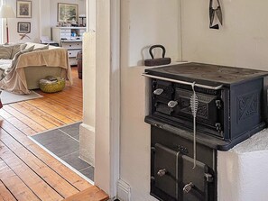 A room with a wooden floor, a bed with a beige cover, a small table, and a vintage stove. - 5 Star Holiday Home in Bjorko (Björkö)