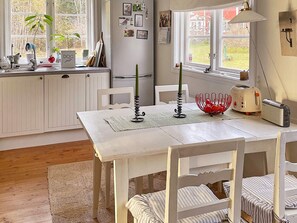A kitchen with a white table, chairs, a toaster, a kettle, and a window with a view of the outside. - 5 Star Holiday Home in Bjorko (Björkö)