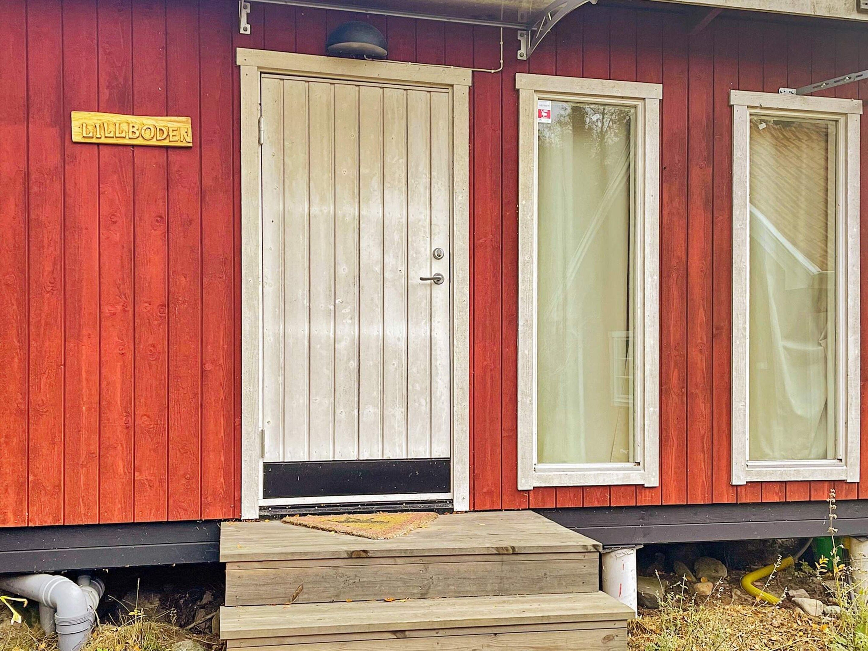 A red wooden building with a beige door and two windows.