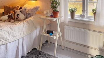 A bedroom with a bed, bedside table, lamp, potted plants, and a radiator.