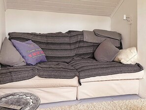 A sofa with a cushion and a pillow with text, a small round table, and a light fixture on the wall. - 5 Star Holiday Home in Bjorko (Björkö)