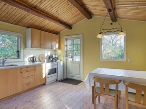 A kitchen with wooden cabinets, a stove, and a dining area with a table and chairs. - 4 Person Holiday Home in Jaegerspris (Jægerspris)
