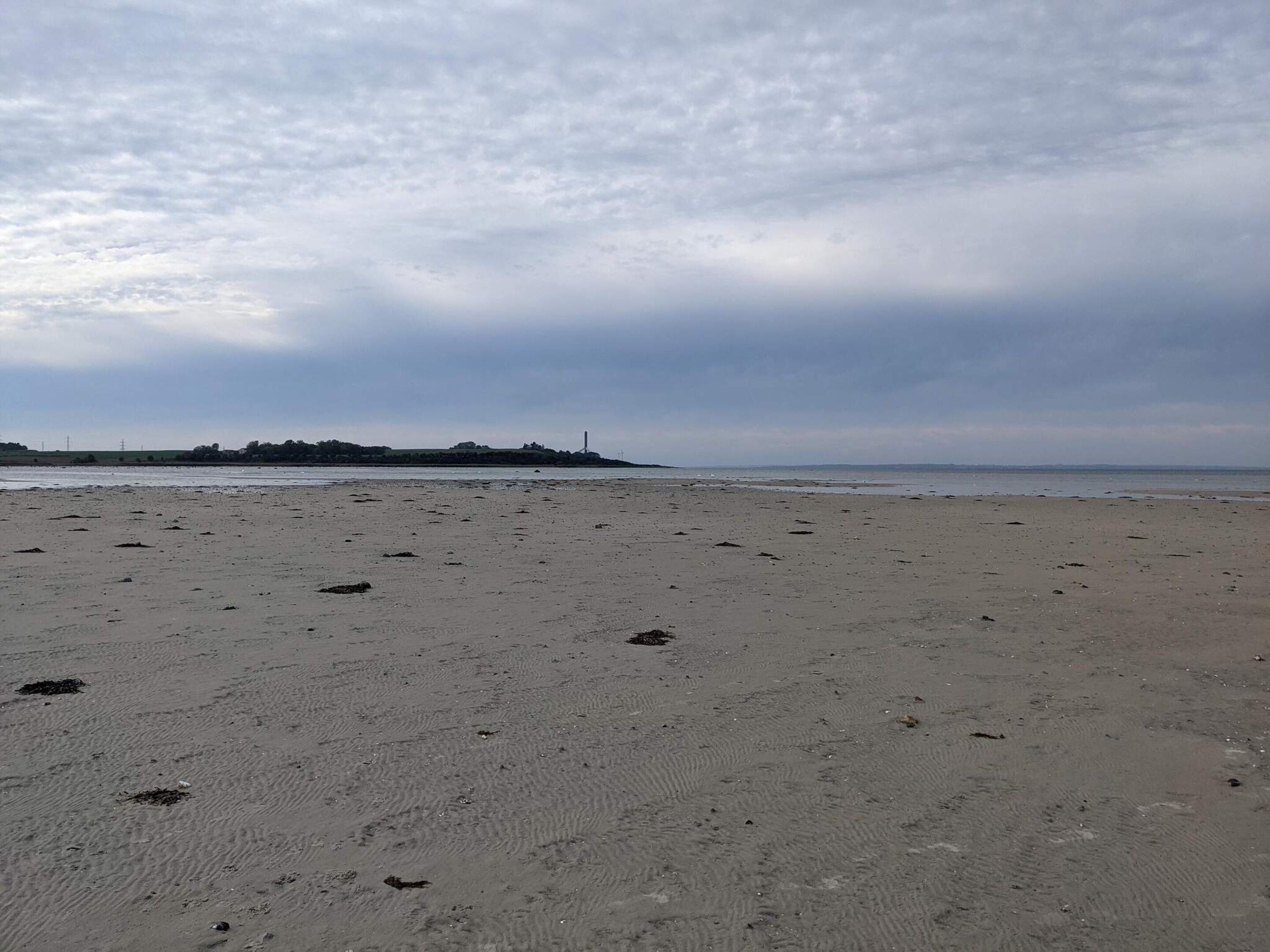 Een breed zandstrand met in de verte een kleine heuvel en een vuurtoren.