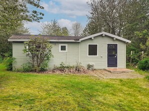 A small, single-story building with a dark-colored door and windows, surrounded by a grassy area and trees. - 4 Person Holiday Home in Jaegerspris (Jægerspris)