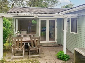 A covered patio area with a wooden table and chairs, a sliding glass door, and a green exterior wall. - 4 Person Holiday Home in Jaegerspris (Jægerspris)
