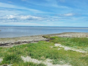 A coastal landscape with a grassy foreground leading to a calm sea under a partly cloudy sky.