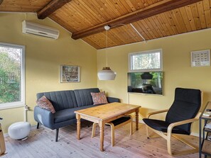 A cozy room with a wooden ceiling, a sofa, a table, and a chair. There are windows and a painting on the wall. - 4 Person Holiday Home in Jaegerspris (Jægerspris)