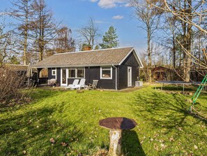 A single-story house with a sloped roof, a front porch with white chairs, and a trampoline in the yard.