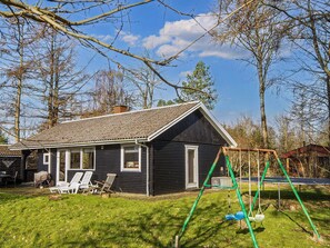 A single-story house with a dark exterior, a sloped roof, and a front porch with two chairs. - 5 Person Holiday Home in Ansager (Ansager)