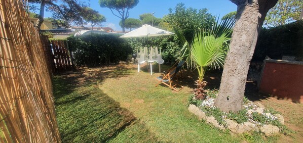 Un patio trasero con una cerca de bambú, una sombrilla blanca y una palmera.