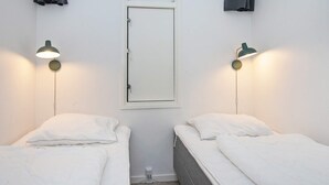 Een kamer met twee enkele bedden, elk met een witte matras en kussen. Aan weerszijden van een deur zijn twee wandlampen bevestigd.