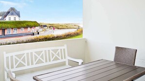 Een balkon met een tafel en rieten stoelen, met uitzicht op een weg en een gebouw met een groen dak.