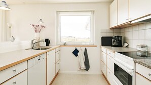 A compact kitchen with white cabinets, a window, a sink, a stove, and a coffee maker.