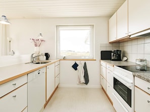 A compact kitchen with white cabinets, a window, a sink, a stove, and a coffee maker. - 4 Star Holiday Home in Hjorring (Hjørring)