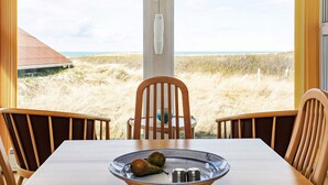 A dining area with a table and chairs, a bowl with fruits, and a view of the beach and dunes. - 4 Star Holiday Home in Hjorring (Hjørring)