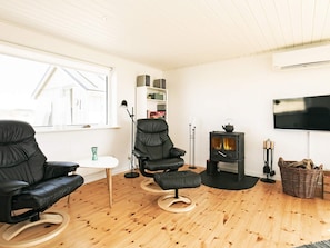 A modern living room with a black leather sofa, a black leather chair, a small white table, a fireplace, a television mounted on the wall, and a wooden floor. - 8 Person Holiday Home in Hjorring (Hjørring)