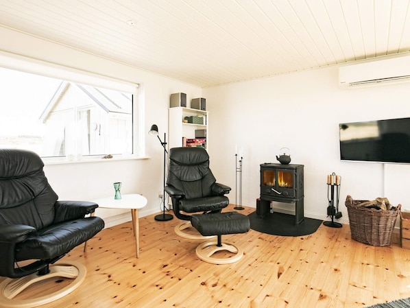 A modern living room with a black leather sofa, a black leather chair, a small white table, a fireplace, a television mounted on the wall, and a wooden floor.