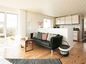 A modern living room with a sofa, a small table, a wicker basket, and a view of the outside. - 4 Star Holiday Home in Hjorring (Hjørring)