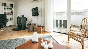 A living room with a fireplace, a TV mounted on the wall, a wicker basket, and a wooden table with vases. - 4 Star Holiday Home in Hjorring (Hjørring)