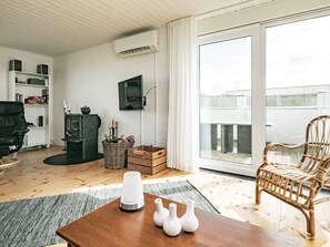 Ett vardagsrum med en öppen spis, en tv som är monterad på väggen, en korg av rotting och ett träbord med vaser.