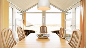 A dining area with a long table, six chairs, a bowl of fruit, and a hanging light fixture.