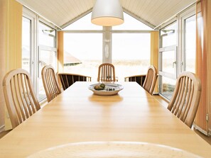 A dining area with a long table, six chairs, a bowl of fruit, and a hanging light fixture. - 4 Star Holiday Home in Hjorring (Hjørring)
