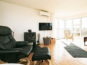 A living room with a black leather sofa, a television, a fireplace, and a wicker chair. - 4 Star Holiday Home in Hjorring (Hjørring)
