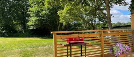A wooden deck with a bench and a table, surrounded by lush greenery and trees.
