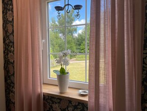 A window with a white pot of white flowers on a wooden ledge, curtains, and a view of a green landscape. - 4 Star Holiday Home in Ljungbyhed (Ljungbyhed)