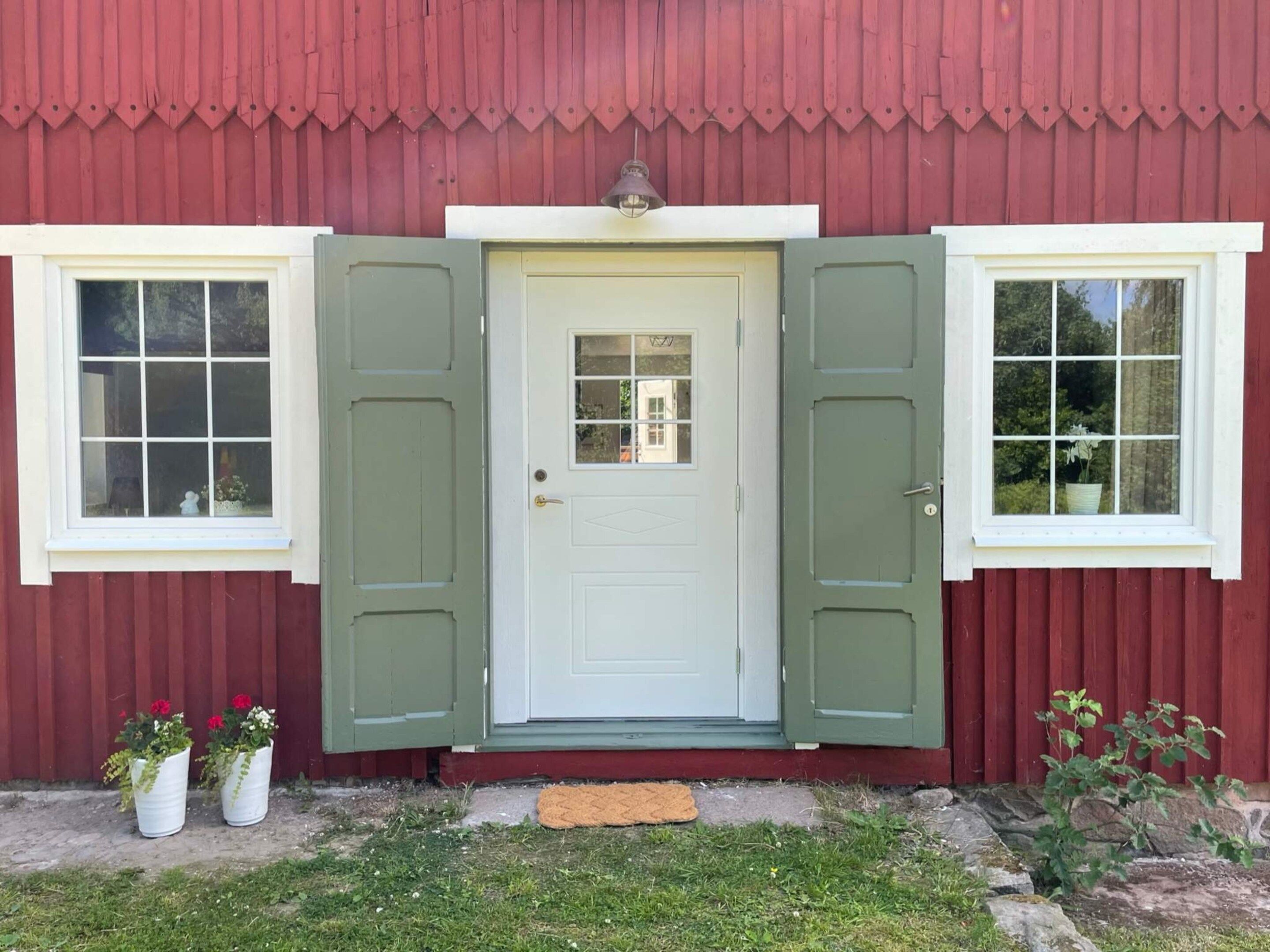 En röd byggnad med en vit dörr, två fönster på vardera sidan och en liten veranda.