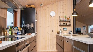 Ett modernt kök med träinredning, en inbyggd ugn och en diskho. På väggen hänger en klocka och på en hylla står köksredskap.
