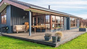 Ett modernt hus med en täckt uteplats, ett trädäck och krukväxter.