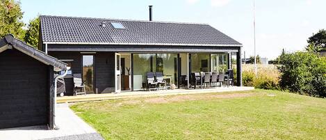 Una casa moderna con un patio, una zona de estar techada al aire libre y una chimenea visible.