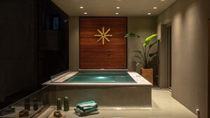 Ein moderner Spa-Bereich mit einer Holzvertäfelung, einer leuchtenden sternförmigen Lampe, einer Glaskuppel-Whirlwanne und einer Pflanze.