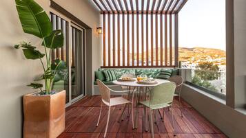 Un balcon avec un plancher en bois, une table avec des chaises, une plante en pot, un canapé avec des coussins et une vue sur un paysage vallonné.