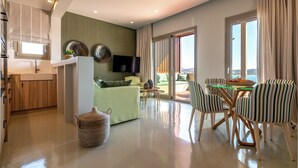 Ein modernes Wohnzimmer mit Sofa, Esstisch und Stühlen, einer Küchenzeile und einem großen Fenster mit Vorhängen.