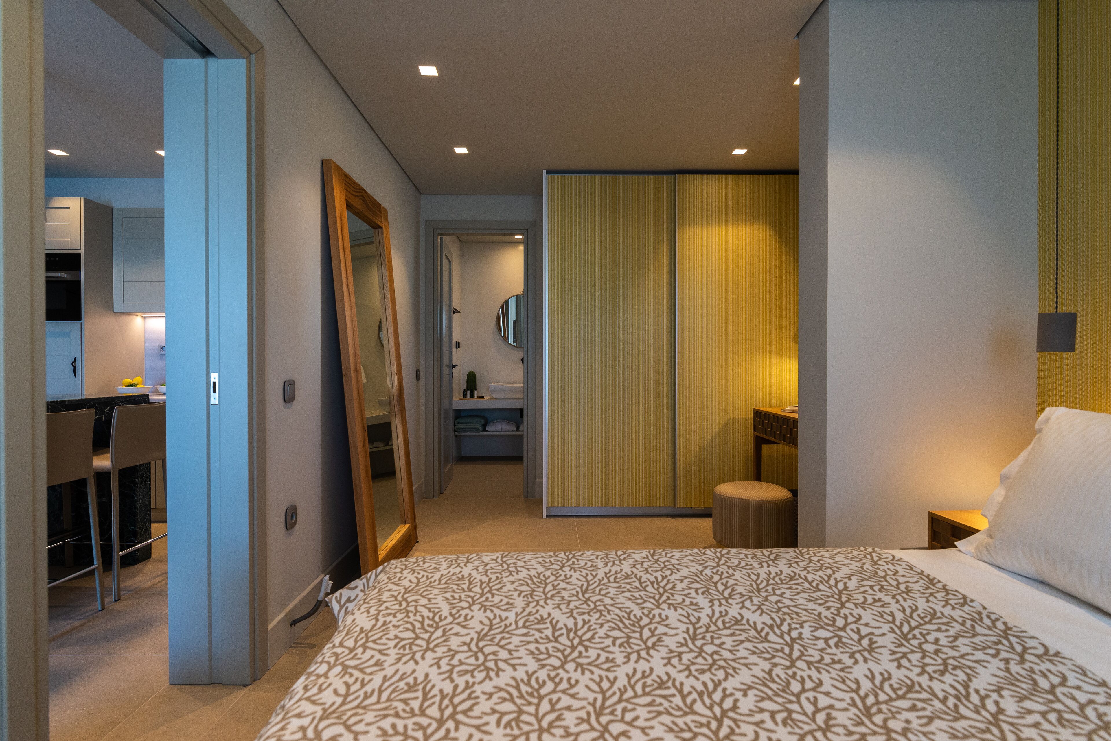 Ett modernt hotellrum med en stor säng, ett skrivbord med en stol, en garderob och ett badrum som syns genom en öppen dörr.