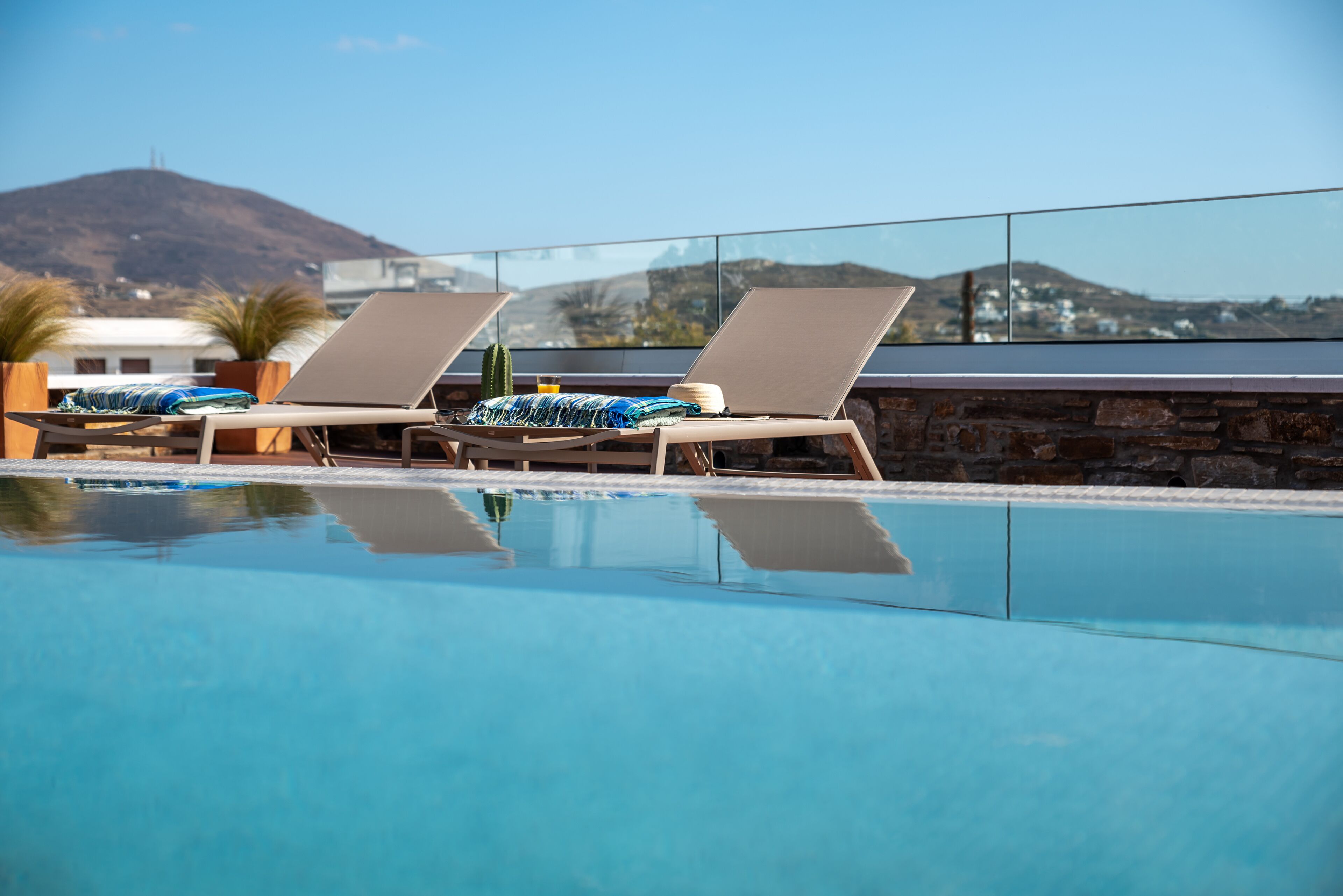 A clear blue pool with two sun loungers and a stone wall.