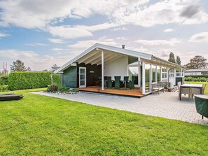 Ett modernt hus med en täckt uteplats, en gräsmatta och en trädgård.