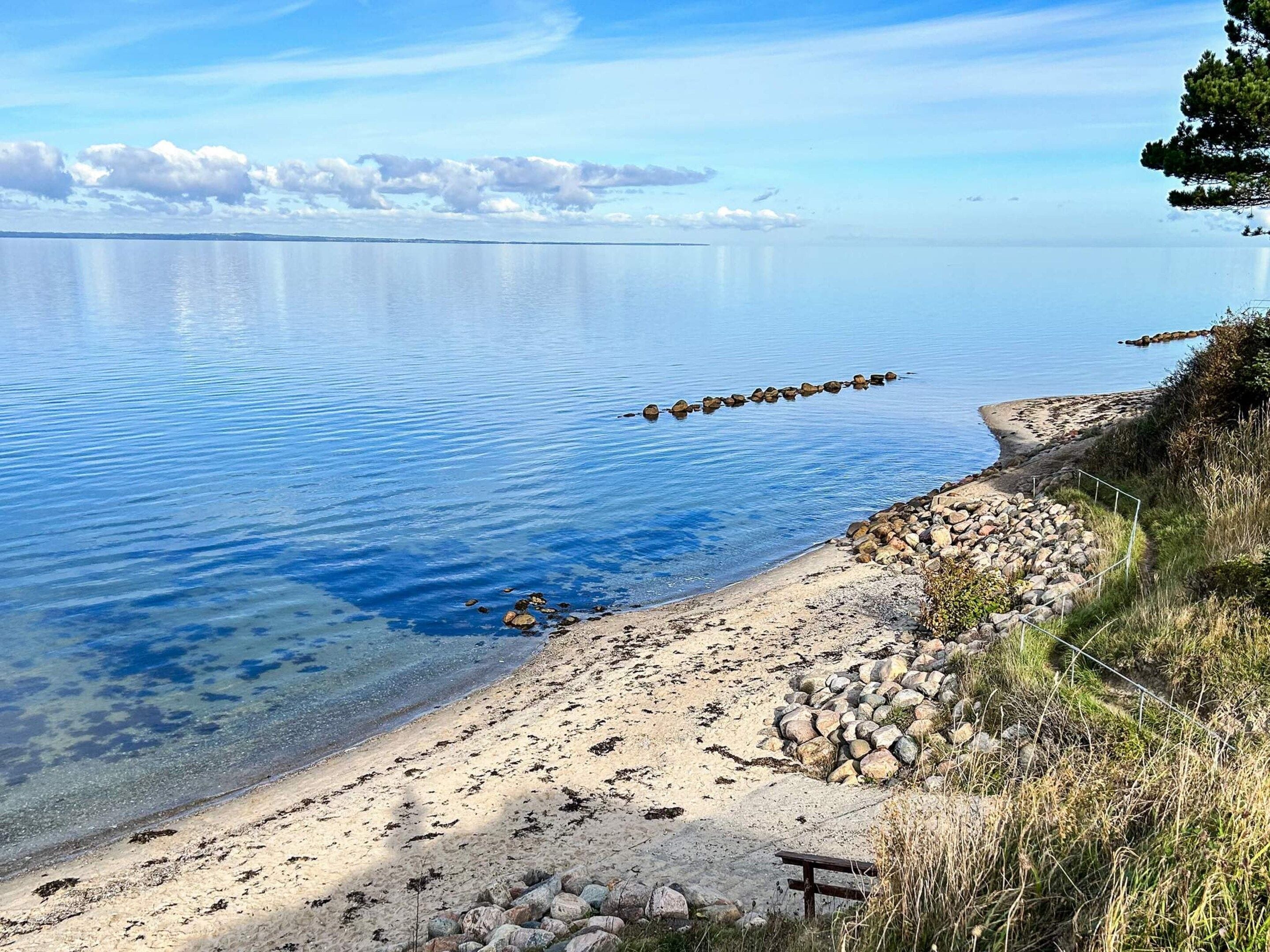 A calm lake with a rocky shoreline and a wooden bench.