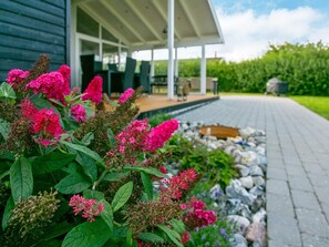Un jardín con vibrantes flores rosadas frente a una casa con porche cubierto.