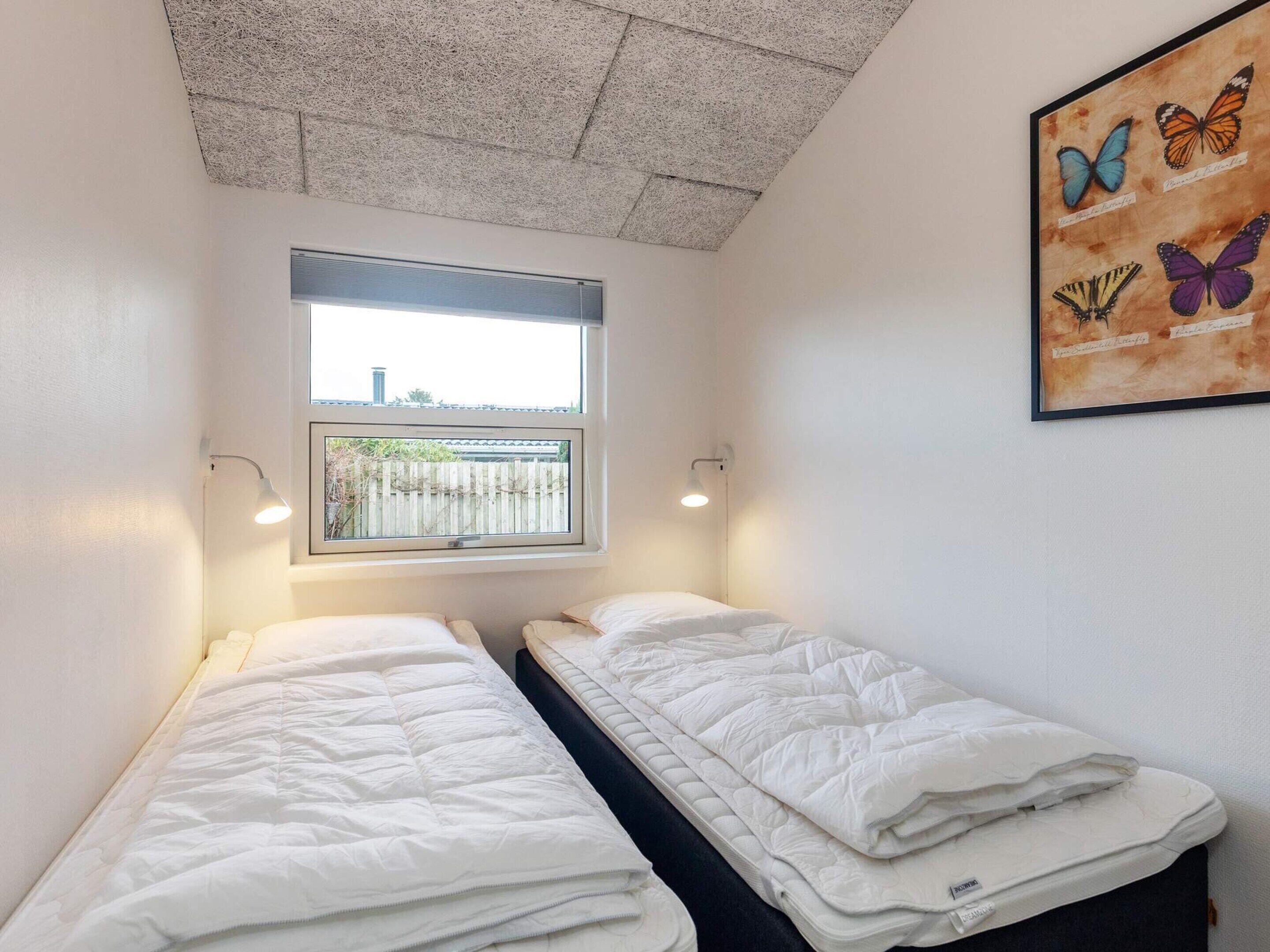 Una habitación con dos camas individuales, una ventana con vistas y una obra de arte con mariposas en la pared.