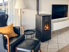A modern living room with a black wood-burning stove, a black leather sofa with a mustard-colored pillow, a small round table, and a floor lamp.