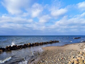 Una playa con piedras, un rompeolas rocoso y el mar.