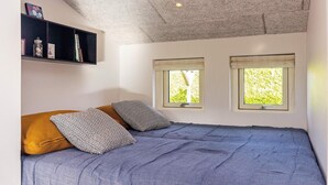 A bedroom with a bed, two windows, a ceiling with a textured finish, and a shelf with books and decorative items.