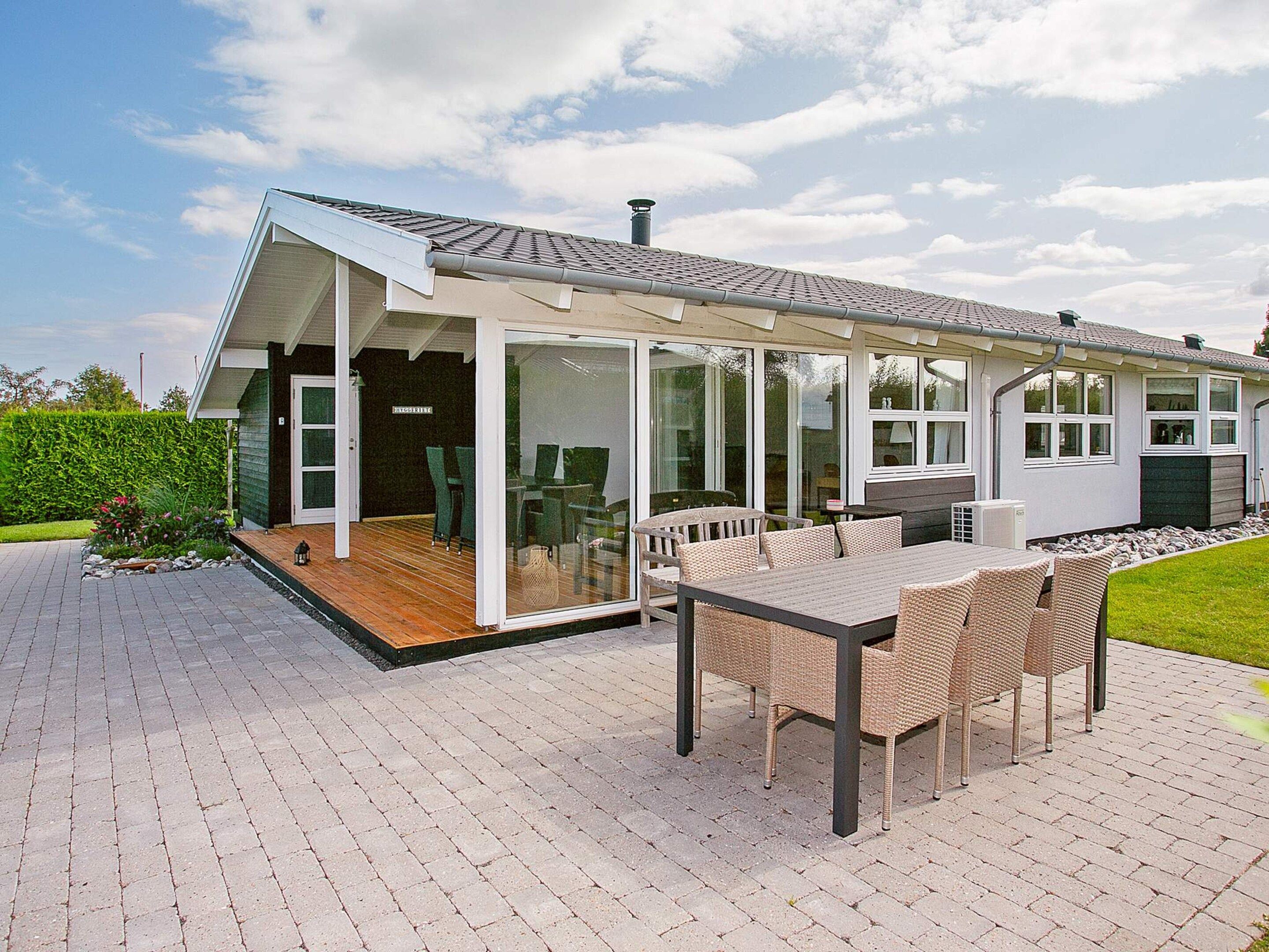 A modern house with a covered patio, a dining area with wicker furniture, and a large window overlooking a garden.