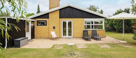 A modern house with a brick exterior, a large sliding glass door, and a patio area with outdoor furniture.