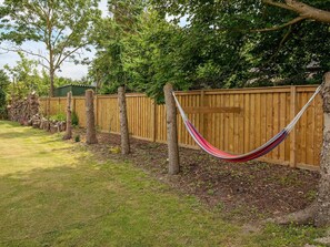 A hammock tied between trees in a backyard with a wooden fence and a stone wall. - 5 Person Holiday Home in Vaeggerlose (Vaeggerlose)